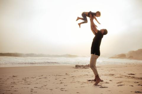 Father tosses young son up in the air while they play on a beach