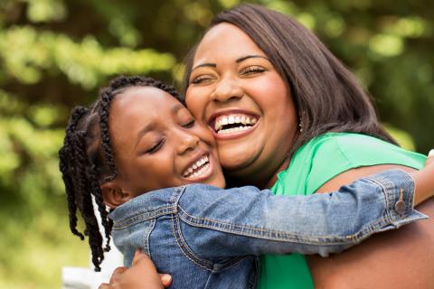 Laughing mother and daughter embrace outside.