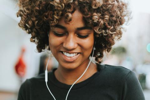Teenaged girl wearing headphones smiles at phone while texting.