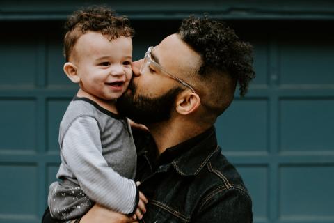 Father holds toddler in his arms while giving him a kiss on the cheek