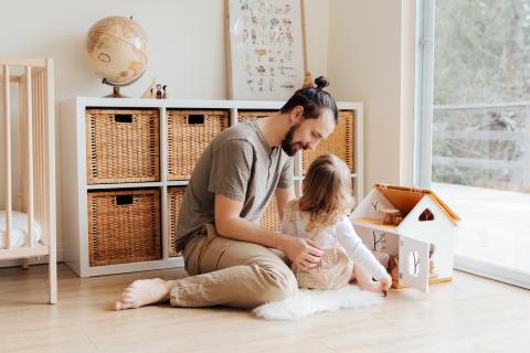 A father and his daughter play together with a doll house.