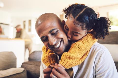 A father is hugged and kissed from behind by his young daughter.