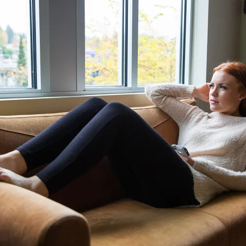 Parent reclines on couch while contemplating a message received on their phone