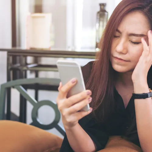 Stressed woman rubs her temple as she looks at her cell phone