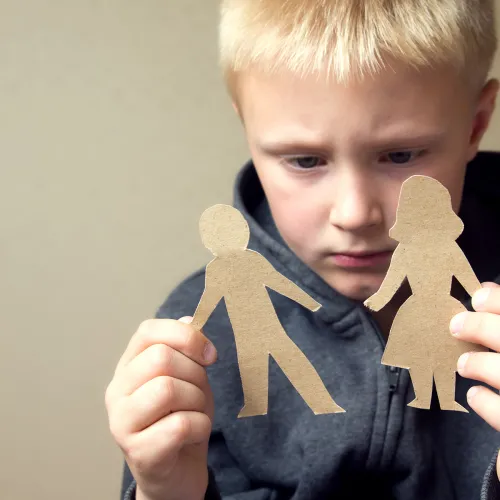 Little boy looks sadly at paper cut-outs of a mom and dad.