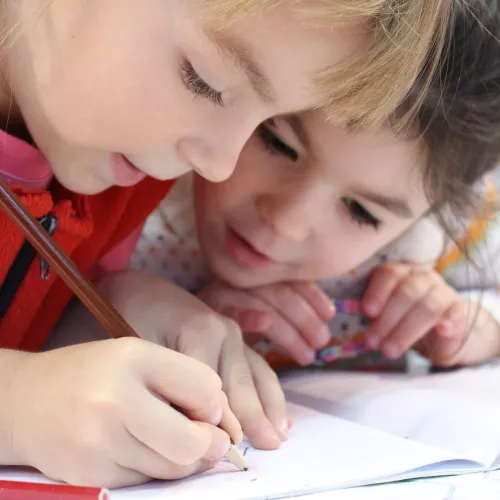 Two children draw together with colored pencils.