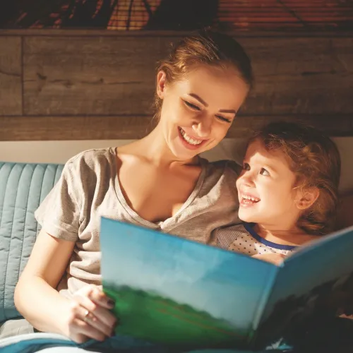 A woman reads a book to her child in bed.