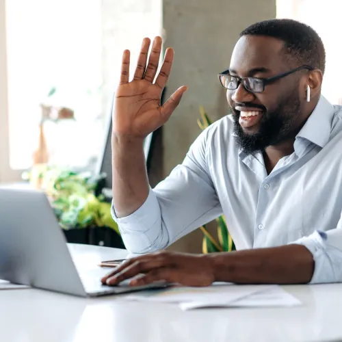 Man in light blue shirt waving to someone on a virtual meeting