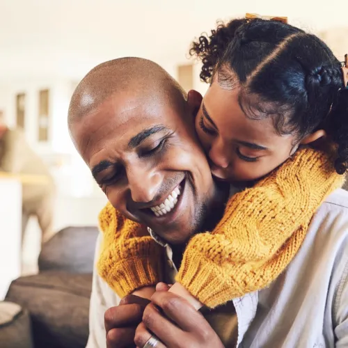 A father is hugged and kissed from behind by his young daughter.