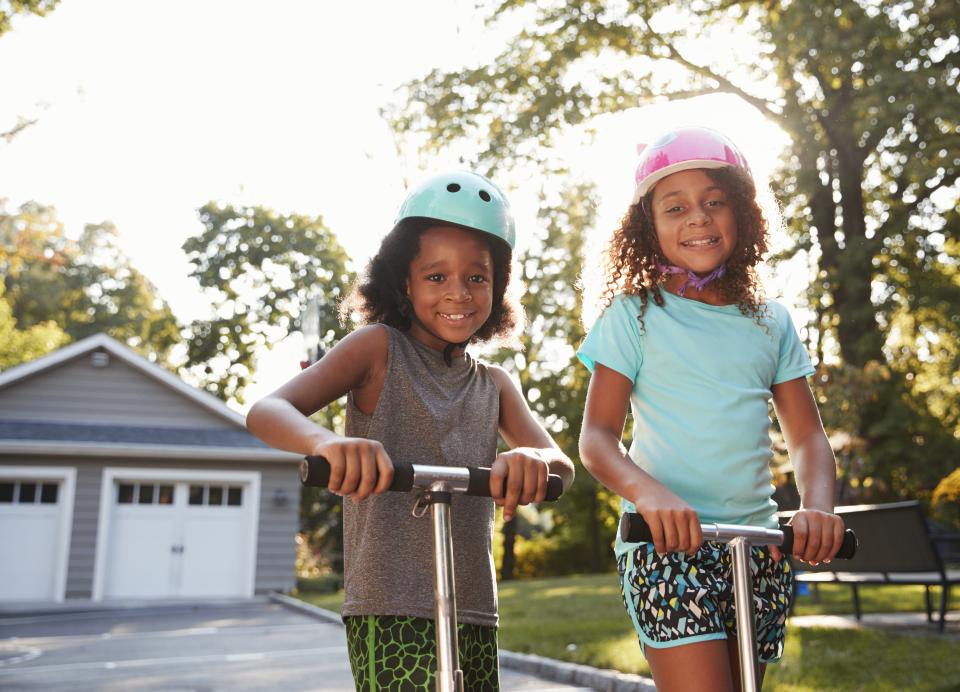 Two young girls playing on scooters in a driveway