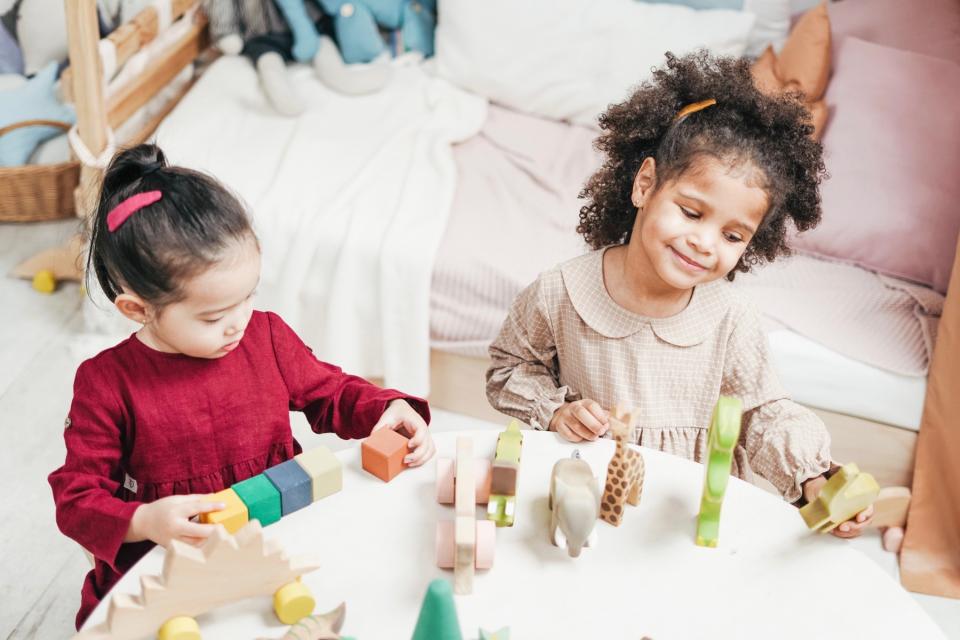 Two girls play with blocks together at a table.