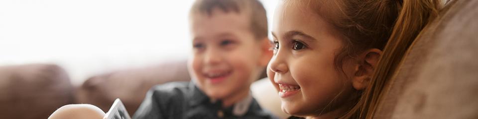 A young brother and sister hang out together on the couch.