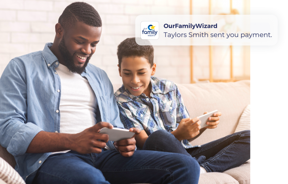 Father and son sit on a couch, each holding a smartphone. The son looks at his Dad's phone to see a push alert about a payment.