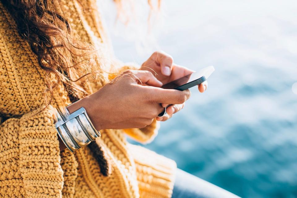 A person with long hair wearing a yellow sweater holds a smartphone in their hands.