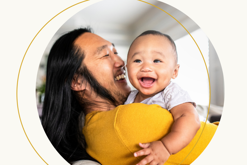 A father holds his infant child and they both smile.