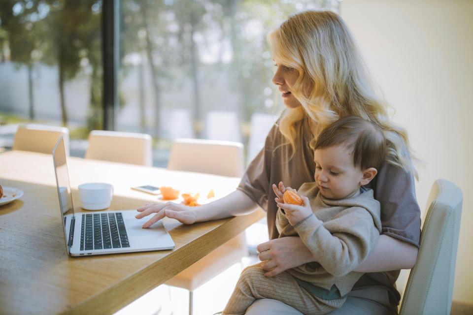 Mom working on laptop while holding baby.